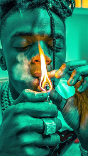 喺青綠色燈光下用打火機點燃大麻煙並呼出煙霧嘅人。 — 深綠色 壁紙