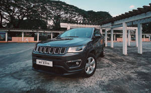 黑色Jeep Compass停放在有蓋結構下，背景有樹木。