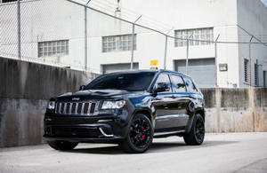 黑色Jeep Grand Cherokee SRT停在工業圍欄和混凝土牆附近。