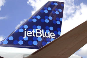 JetBlue 飛機尾翼特寫，帶有藍色波點，背景是藍天和白雲。