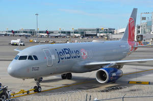 JetBlue 飛機停泊在機場閘口，可見客運大樓和地勤設備。