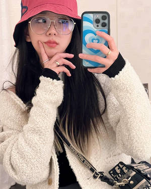 戴粉紅色帽子和眼鏡的年輕女性用手機對著鏡子自拍
