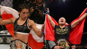 兩名女性MMA冠軍在八角籠中手持旗幟和腰帶慶祝勝利。