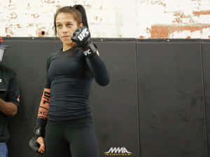 身穿黑色裝備的女性MMA拳手在訓練健身室戴著手套擺姿勢。