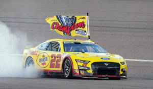 黃色NASCAR賽車以煙霧和旗幟慶祝冠軍。