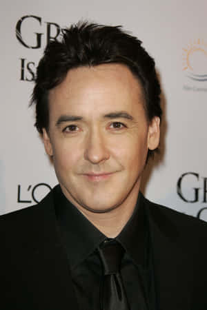John Cusack 穿著黑色西裝和領帶在正式活動中。 — 里維·阿卡曼 GIF 壁紙