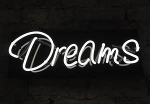 一個發光的白色霓虹燈牌，上面寫着 'Dreams'，安裝在深色磚牆上。