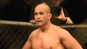 一位光頭MMA戰士在黑色八角籠內，身後有一名攝影師。