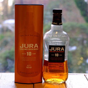 Jura 10年威士忌酒瓶和盒子放在窗邊的木桌上。 — 最佳 壁紙