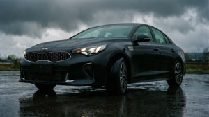 黑色Kia轎車停在濕漉漉的路面上，頭頂是烏黑的暴風雲，車頭燈亮著