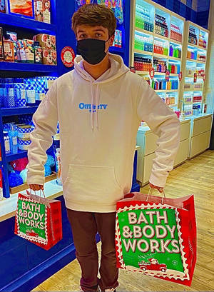 年輕男子戴著口罩，在商店裡拿著Bath & Body Works節日購物袋。