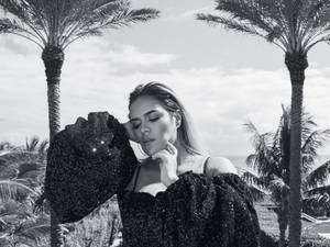 身穿閃亮黑色連衣裙的女性在戶外棕櫚樹間擺姿勢。