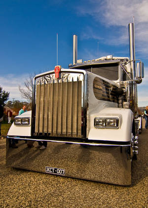 鍍鉻白色Kenworth半掛卡車停在碎石路上，附近有人。