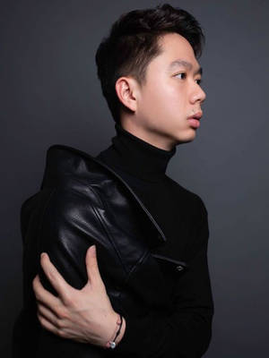 身穿黑色皮褸和高領毛衣的年輕男子在攝影棚中手放在肩膀上站立。 — 黑色 壁紙