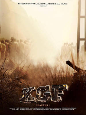 KGF Chapter 1 的電影海報，以夕陽下塵土飛揚的田野中的槍支和人群為特色。 — 電影 壁紙