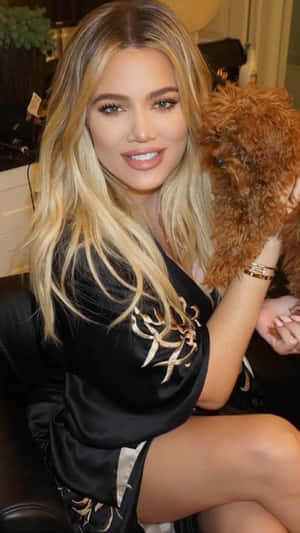 Khloé Kardashian 喺室內穿著黑色絲質長袍，抱住一隻毛茸茸嘅啡色狗。 — 考特妮·卡達夏 壁紙