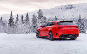 紅色Kia Stinger GT停泊在雪地冬季景觀中，背景有松樹和山脈。
