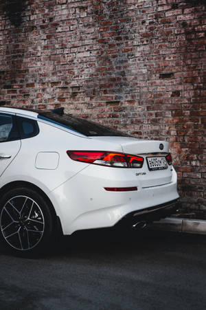 白色Kia Stinger夜間停泊在磚牆旁。