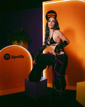 穿著前衛黑紫色服裝的女性在Spotify活動中，在發光的橙色牆前擺姿勢。