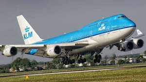 KLM波音747從跑道起飛，附近有房屋和綠色田野。
