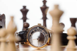 棋盤上的奢華金色手錶，周圍有模糊的棋子。