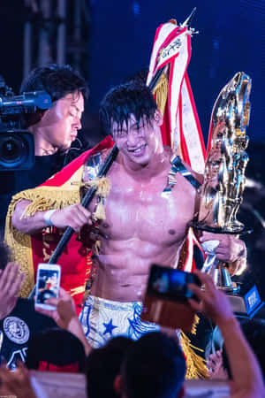 摔角手在舞台上捧著獎盃和冠軍腰帶慶祝勝利。