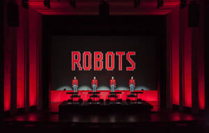 四位身穿紅色外套的演員在舞台上，身後有一個紅色發光的「ROBOTS」標誌。 — 音樂 GIF 壁紙