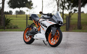 白色和橙色KTM RC電單車停在鋪砌道路旁，靠近樹木。
