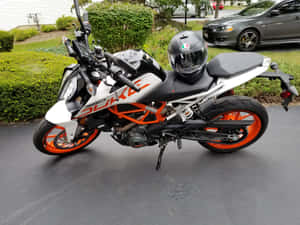 白色和橙色的KTM 390 Duke電單車停在濕路面上，座位上有頭盔。 — 機車 壁紙