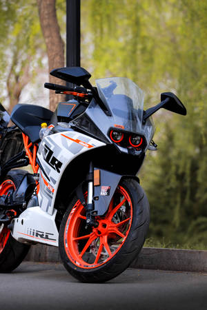時尚的KTM RC電單車，橙色車輪，停在戶外樹旁。 — 機車 壁紙