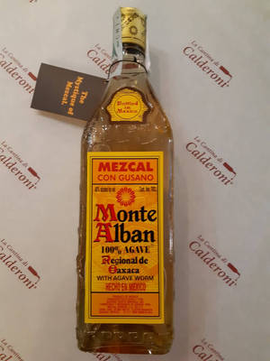 一瓶有龍舌蘭蟲的 Monte Alban 梅斯卡爾酒，放在有品牌標誌的紙上。
