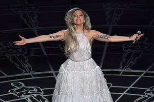 Lady Gaga 身穿白色長袍在舞台上表演，雙臂伸展。