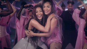 兩名女性在粉紅色主題的舞台表演中擁抱並微笑。