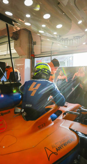 F1車手在橙色賽車中，車庫工作人員在日落時分。