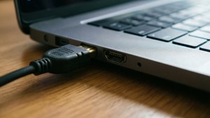 黑色HDMI線連接到銀色手提電腦，置於木質表面