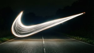 一條明亮的Nike標誌形狀的光跡在夜間橫跨黑暗的道路。