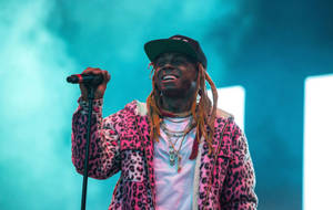 身穿粉紅色豹紋外套的說唱歌手微笑著在舞台上拿著麥克風。 — Lil Wayne 壁紙