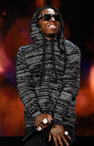 饒舌歌手戴太陽眼鏡和連帽衫在舞台上握麥克風 — Lil Wayne 壁紙