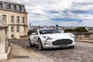 白色Aston Martin跑車在巴黎屋頂上，享有城市景觀。 — MacBook Air 13 壁紙