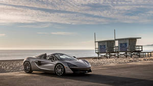 銀色McLaren跑車停泊在日落時分海灘道路旁的救生員瞭望塔附近。
