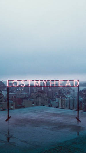 粉紅色霓虹燈牌，上面寫著 lostmyhead，在一個濕漉漉的屋頂上，俯瞰著黃昏時分的城市。 — 霓虹美學 壁紙
