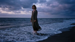 女人在暴風雨天空下赤腳站在暮色海灘的海洋波浪中