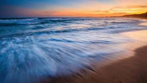 絲滑的海浪在充滿活力的日落地平線上沖刷著金色沙灘。