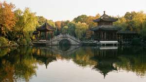 石橋連接水上亭閣，秋樹與倒影