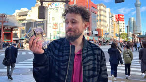 男子在繁忙的東京街道上手持日本日元紙幣，背景為晴空塔。