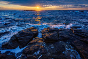 夕陽下的海洋，海浪拍打黑色岩石