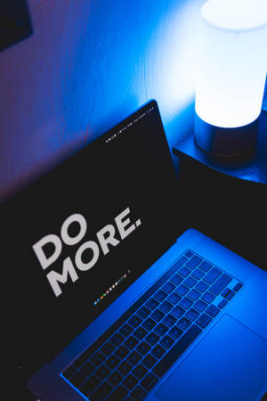 夜晚藍色燈光下手提電腦屏幕顯示 'DO MORE.'。