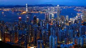 黃昏時分的香港城市景觀，燈火通明的摩天大樓與港灣水面。