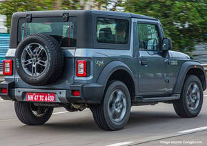 灰色鈴木 Jimny SUV 在鋪砌道路上行駛，周圍綠意盎然。