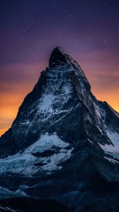 在帶有紫色和橙色色調的星空暮色天空下的雪山山峰。